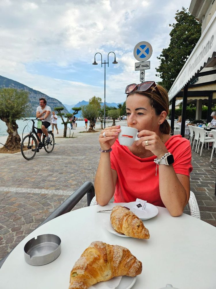Magdalena pije espresso przy stoliku z cornetti, w tle promenada nad jeziorem